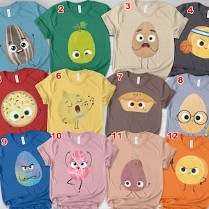 May include: A collection of colorful t-shirts featuring whimsical food-themed cartoon characters. Designs include a sunflower, avocado, egg with a mustache, basketball emoji, donut, singing onion, pie, egg with glasses, angry egg, dancing egg, potato, and a sun.