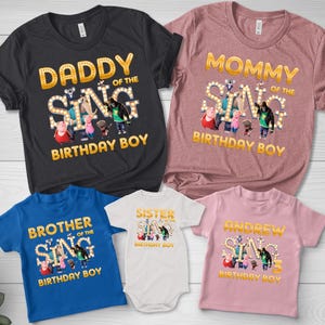 May include: A collection of themed t-shirts and a onesie. The shirts are in various colors, including black, pink, blue, and white. Each shirt features the text "Daddy of the Sing Birthday Boy", "Mommy of the Sing Birthday Boy", "Brother of the Sing Birthday Boy", "Sister of the Sing Birthday Boy", and "Andrew Sing Birthday Boy".