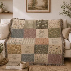May include: A woven throw blanket featuring a patchwork design of floral patterns, butterflies, and gingham squares. Several blocks contain printed Bible verses including Psalm 46:10, Philippians 4:13, Lamentations 3:23, Psalm 23:1, and Psalm 139:14. The blanket has fringed edges.