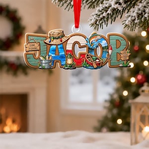 May include: A hanging Christmas ornament shaped like the name JACOB in large letters. The design features a fishing hat, a bucket of fish, a lantern, a jumping fish, a red boat, and wooden signs reading GONE FISHING and LAKE FISHING CAMP.
