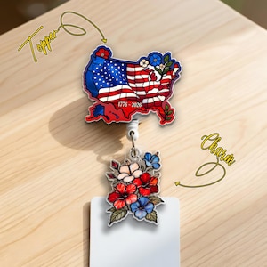 May include: A patriotic badge reel featuring a map of the United States with the American flag design and the text "1776-2026". The charm includes a floral design with red, white, and blue flowers.