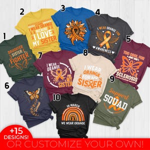May include: Collection of t-shirts in various colors, each featuring orange ribbon designs and text related to awareness and support. Designs include phrases like "I wear orange," "Support Squad," and "Daughter Sister Fighter."