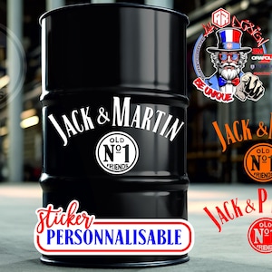 Peut inclure: Un fût en métal noir arborant un motif graphique blanc avec le texte Jack & Martin et Old No 1 Friends. Des options de texte supplémentaires incluent Jack & Nom et Jack & Prenom en orange et rouge, avec une étiquette sticker personnalisable.