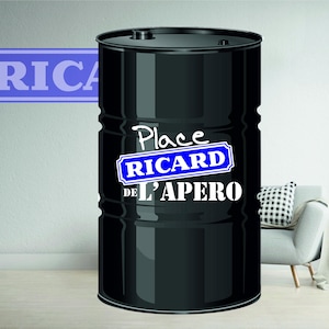 Peut inclure: Un baril métallique noir avec le texte "Place RICARD DE L'APERO" en blanc et bleu. Un panneau avec le mot "RICA" est visible en arrière-plan. Le baril est dans une pièce avec une chaise et une plante.
