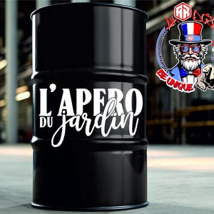May include: A black cylindrical metal drum featuring the white text L'APERO DU JARDIN printed on the front. The surface is smooth and glossy with horizontal ridges. A circular logo with a bearded character in a top hat is visible in the upper right.