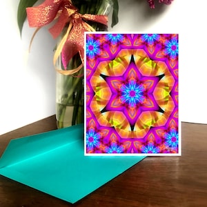 May include: A colorful, abstract card with a pink, yellow, and blue geometric pattern. The pattern is symmetrical and has a star-like shape in the center.