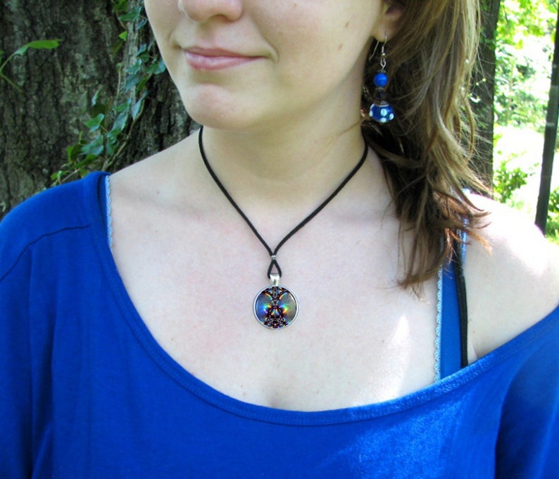 May include: A woman wearing a blue shirt with a black choker necklace and a round pendant with a colorful design. She is also wearing blue and white earrings.