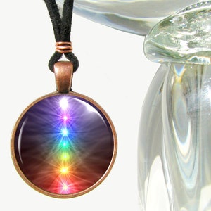 May include: A copper pendant necklace with a round glass charm featuring a colorful chakra symbol. The charm has a dark background with seven glowing chakras in rainbow colors.