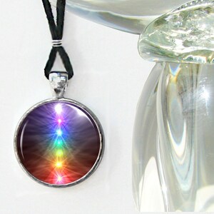 May include: A silver pendant necklace with a round glass charm featuring a colorful seven-chakra symbol. The chakra symbol is a vertical line of seven overlapping circles, each a different color of the rainbow, with a star in the center of each circle.