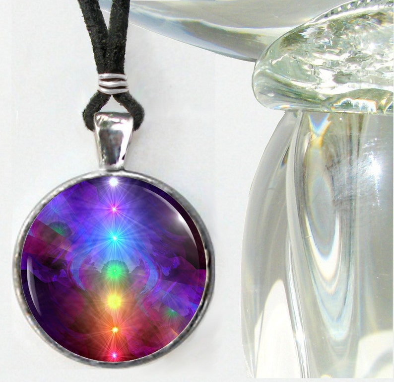 May include: A round silver-toned pendant necklace featuring a black cord and a glass cabochon display. The circular insert showcases a vertical alignment of glowing, starburst-like light points in red, orange, yellow, green, blue, and violet hues.