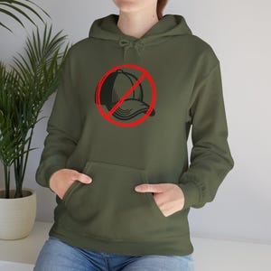 Puede incluir: Sudadera con capucha verde oliva con bolsillo delantero y capucha con cordón. El gráfico en la parte delantera presenta una gorra de béisbol negra dentro de un círculo rojo con una línea roja que lo atraviesa, un símbolo de prohibición.