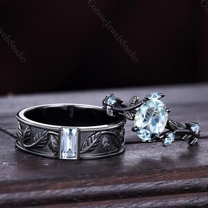 May include: Two rings, one with an oval-cut light blue gemstone and a floral design, the other with a rectangular gemstone and leaf pattern. The rings are set on a dark wooden surface.