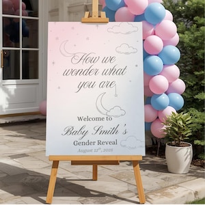 Puede incluir: Un caballete de madera muestra un letrero con el texto "How we wonder what you are" y "Welcome to Baby Smith's Gender Reveal August 12th, 2025." El letrero tiene un fondo degradado rosa y azul con ilustraciones de nubes y luna. Un arco de globos rosas y azules está a la derecha.