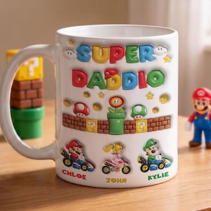 Puede incluir: Taza de cerámica blanca con temática de Super Mario, con el texto "SUPER DADDIO" en letras 3D coloridas. La taza incluye personajes de Mario en karts y nombres debajo. Un regalo divertido para un papá.
