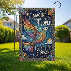 May include: A garden flag featuring a colorful dove with rainbow wings, set against a dark blue starry sky. The flag has the words "Imagine All The People Living Life In Peace" and is decorated with flowers and peace signs.