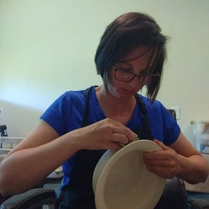Może przedstawiać: Osoba w niebieskiej koszuli i czarnym fartuchu trzyma białą ceramiczną miskę. Miska jest okrągła i ma gładką powierzchnię.