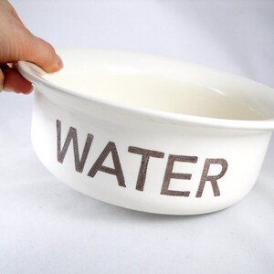 K&ouml;nnte beinhalten: Wei&szlig;e Keramiksch&uuml;ssel mit dem Wort "WATER" in Grau auf der Seite.
