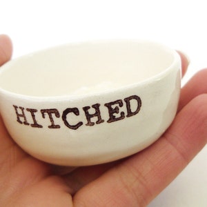 May include: White ceramic dish with the word "HITCHED" written in black lettering.
