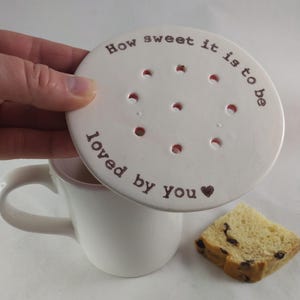 May include: White ceramic mug with a white ceramic lid that says "How sweet it is to be loved by you" with a heart. The lid has holes for tea or coffee.