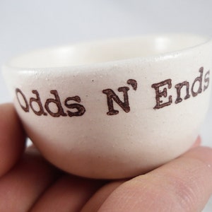 May include: White ceramic bowl with the words "Odds N' Ends" printed in brown lettering.