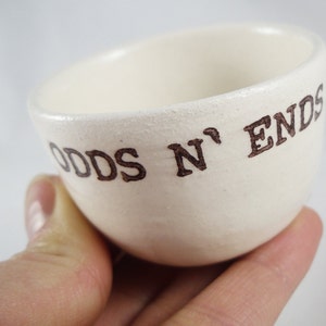 May include: White ceramic bowl with the words "Odds N' Ends" written in brown lettering.