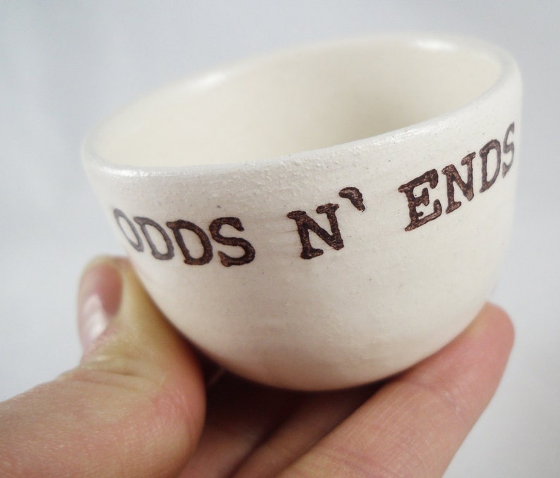 May include: White ceramic bowl with the words "Odds N' Ends" written in brown lettering.