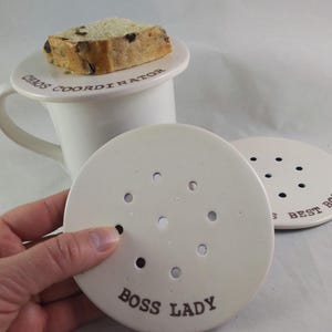 Peut inclure: Trois couvercles de tasse en céramique blanche avec des trous. Les couvercles portent les inscriptions "Chaos Coordinator", "Boss Lady" et "Best Boss".