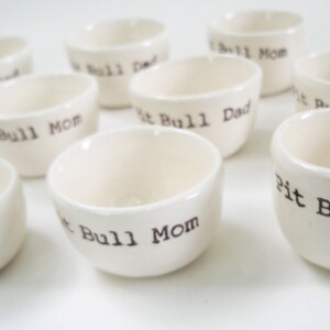 May include: A set of ten white ceramic bowls with black lettering. The bowls are labeled with the words "Pit Bull Dad", "Pit Bull Mom", and "Pit Bull".