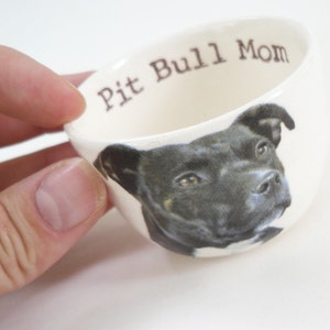 May include: White ceramic cup with a black and white image of a pit bull dog and the text "Pit Bull Mom" printed on the side.