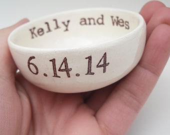 May include: White ceramic ring dish with the text "Kelly and Wes 6.14.14" inscribed on the bottom.