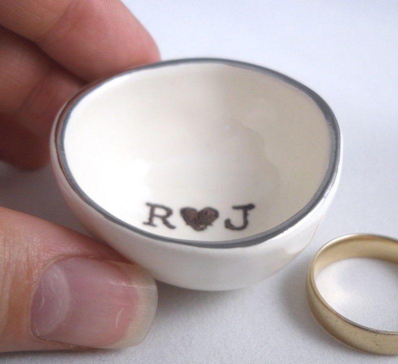 May include: White ceramic ring dish with a silver rim and the initials "R&J" with a heart in between.