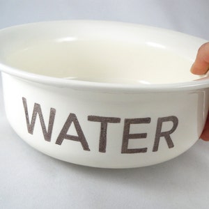K&ouml;nnte beinhalten: Wei&szlig;e Keramiksch&uuml;ssel mit dem Wort "WATER" in Grau auf der Seite.