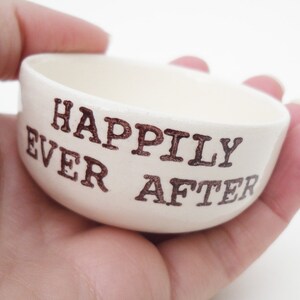 May include: White ceramic ring dish with the words "Happily Ever After" written in brown lettering.