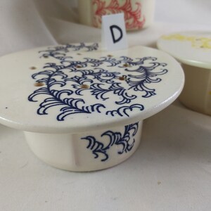 May include: A white ceramic dish with a blue floral design and a matching base. The dish has a letter "D" on a white card in front of it.
