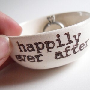 May include: White ceramic ring dish with the words "happily ever after" printed in black.