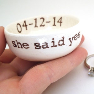 Puede incluir: Plato de cerámica blanco para anillos con el texto "04-12-14 she said yes" en letras marrones.