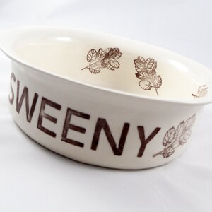 May include: White ceramic bowl with brown leaf designs and the word "SWEENY" printed on the side.