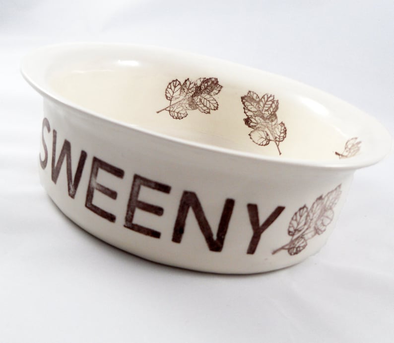 May include: White ceramic bowl with brown leaf designs and the word "SWEENY" printed on the side.