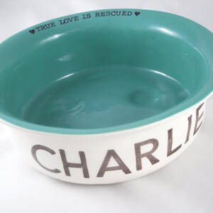 May include: White ceramic pet bowl with a teal blue interior. The bowl has the words "TRUE LOVE IS RESCUED" in black lettering on the rim and the name "CHARLIE" in black lettering on the bottom.