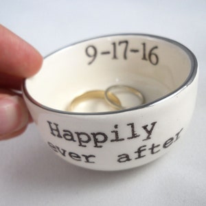 May include: White ceramic ring dish with a silver rim. The dish has the words "Happily ever after" and the date "9-17-16" printed on it.