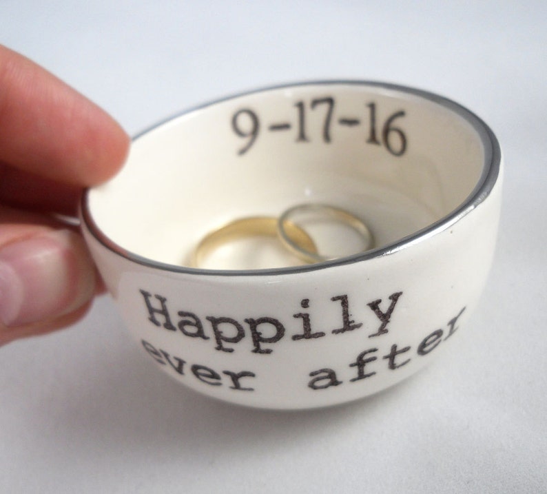 May include: White ceramic ring dish with a silver rim. The dish has the words "Happily ever after" and the date "9-17-16" printed on it.