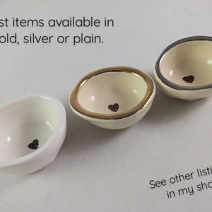 May include: Three small white ceramic bowls with a heart design. The bowls are available in gold, silver, or plain.