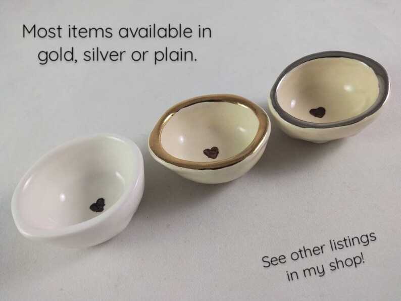 May include: Three small white ceramic bowls with a heart design. The bowls are available in gold, silver, or plain.