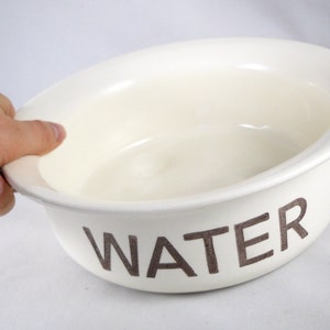 K&ouml;nnte beinhalten: Wei&szlig;e Keramiksch&uuml;ssel mit dem Wort "WATER" in Braun auf der Seite.