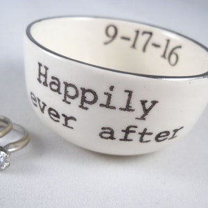 May include: White ceramic ring dish with a silver rim. The dish has the words "Happily ever after" and the date "9-17-16" printed on it.