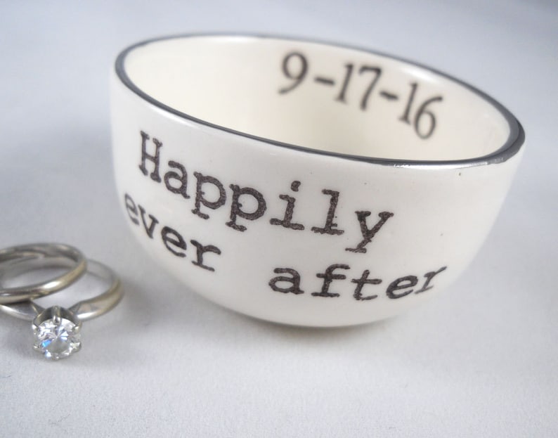 May include: White ceramic ring dish with a silver rim. The dish has the words "Happily ever after" and the date "9-17-16" printed on it.