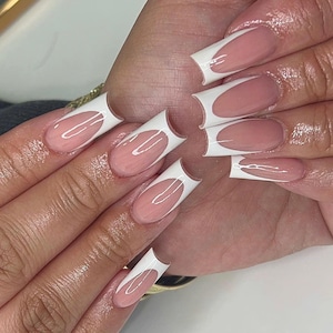 Puede incluir: Una mano que muestra uñas acrílicas largas y cuadradas. Cada uña presenta una base rosa pálido con un diseño de punta francesa blanca. Las uñas son brillantes y están bien cuidadas, mostrando un estilo clásico y elegante.