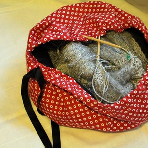 May include: Red and white polka dot drawstring bag with a gray knitted scarf inside. The bag has black drawstrings and a black strap.