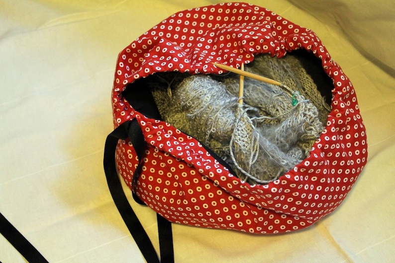 May include: Red and white polka dot drawstring bag with a gray knitted scarf inside. The bag has black drawstrings and a black strap.