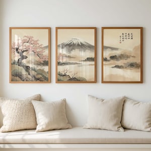 May include: Three framed landscape prints with a Japanese aesthetic. The artwork features a mountain, cherry blossoms, and misty scenery in muted tones. The frames are a warm brown, and the prints hang above a bench with pillows.